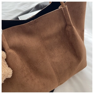 Détail d'un sac cabas en daim marron avec surpiqûres et un charme d'ours en peluche