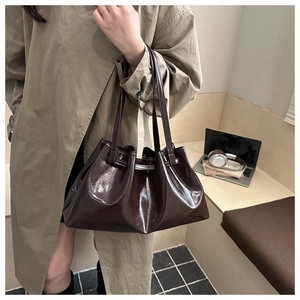 Close-up of a glossy dark brown pleated bucket bag with long handles in a lifestyle setting
