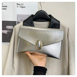 Detail of silver metallic envelope clutch bag with an oval gold buckle held by hand