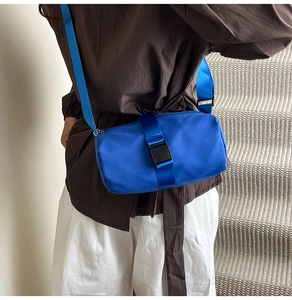 Blue cylindrical travel crossbody bag with wide strap and plastic buckle on model