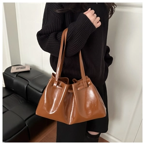 Macro shot of brown glossy pleated bucket bag showing polished PU leather texture