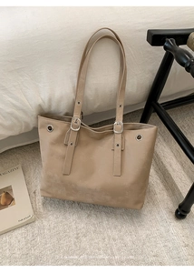 Detail of beige suede tote bag showing silver metal eyelets and adjustable buckle strap