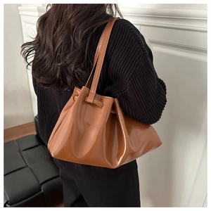 Detail of a brown glossy leather bucket bag with drawstring pleats and slim strap