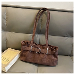 Close-up of brown suede shoulder bag featuring a silver metal buckle on a gray leather sofa