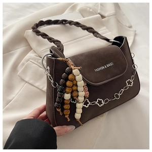 Macro shot of dark brown textured leather bag with floral silver chain and wood bead tassel