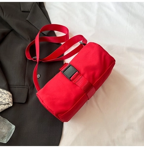 Detail of red cylindrical travel bag with adjustable strap and buckle on black blazer