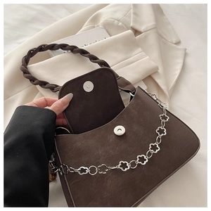 Detail of dark brown leather underarm bag with woven handle and flower metal chain link
