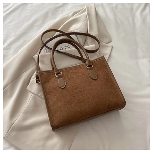 Dettaglio borsa tote in pelle scamosciata marrone con trifogli su blazer bianco