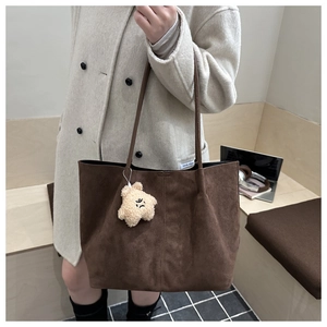 Détail d'un sac cabas en daim marron avec de fines anses et un pendentif ours en peluche
