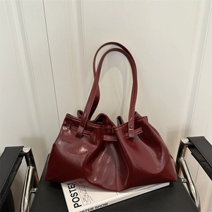 Glossy burgundy pleated leather tote bag on black chair with magazine, shoulder view