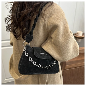 Detail of black suede shoulder bag featuring silver floral chain and woven strap on model