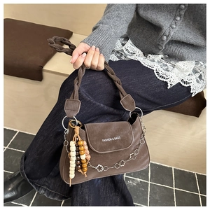 Detail of a brown vintage leather shoulder bag with woven strap and ethnic wooden bead charm