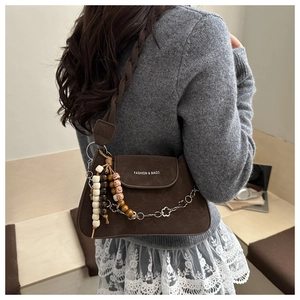 Detail of brown nubuck shoulder bag with woven strap, beads and metallic flower chain