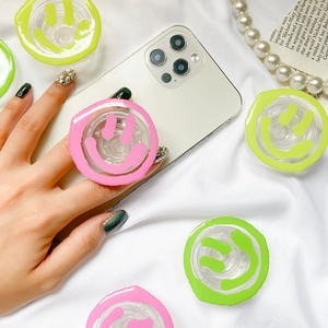Detail of neon green and pink smiley face phone socket grips on a white smartphone