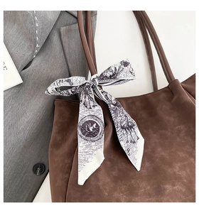 Close-up of black and white printed silk scarf tied on a brown tote bag handle