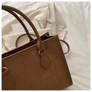 Dettaglio borsa shopper marrone scuro con motivo a quadrifoglio a rilievo e texture scamosciata
