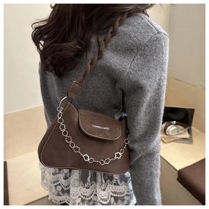 Detail of dark brown leather crossbody bag with braided strap and silver floral chain link