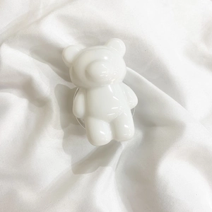 Close-up of a minimalist white glossy bear-shaped phone grip on a white fabric background
