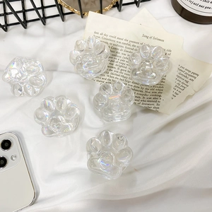 Detail of six transparent aurora laser cat paw phone grips on a white fabric background
