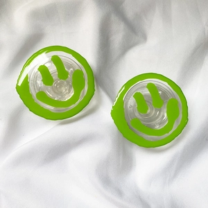 Detail view of two transparent acrylic phone grips with 3D green smile patterns