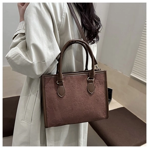 Dettaglio borsa shopper marrone con motivi a quadrifoglio su trench beige