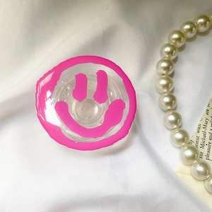Close-up of a pink smile face transparent phone grip on a white fabric background