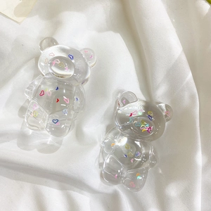 Close-up of clear bear-shaped phone grip with colorful heart patterns on white fabric