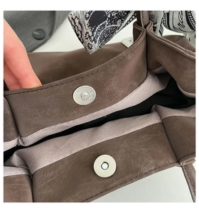 Detail of brown faux suede tote bag featuring magnetic buckles and printed silk scarf handle