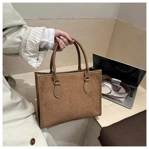 Dettaglio del motivo a trifoglio goffrato su borsa tote in pelle marrone da ufficio