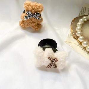 Detail of plush bear phone socket with plaid bow on a white textured fabric background