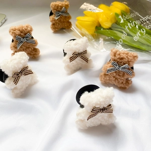 Close-up of plush bear hair clips in brown and white with checkered bows on white fabric