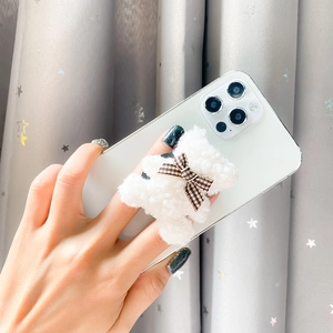 Close-up of a plush white teddy bear phone socket with a brown plaid bow on a smartphone