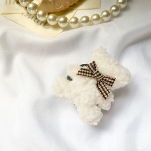 Close-up of white plush bear hair claw clip with brown plaid bow on a white fabric background