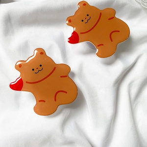 Close-up of two cute brown bear acrylic phone grips on a soft white fabric background