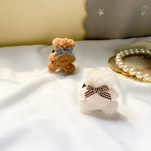 Detail of plush bear phone accessory with lamb wool texture and a black white plaid bow