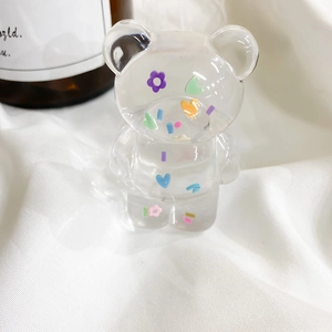Detail of transparent bear phone grip with colorful sequins on white knitted fabric