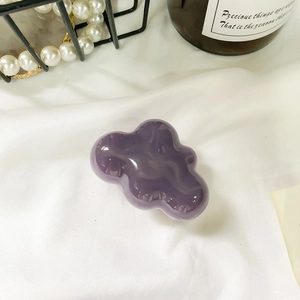 Detail view of a purple cloud shaped phone stand on white satin with pearl jewelry