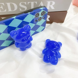 Close-up of translucent Klein blue 3D bear pop socket and checkered phone case on silk