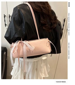Detail of pink baguette bag featuring decorative white lace bow and long silk ribbons
