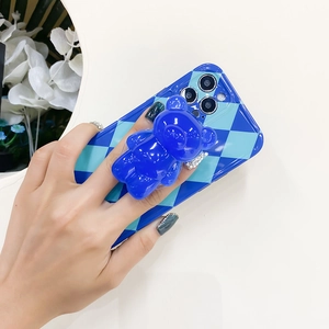 Blue rhombic phone case with a 3D bear pop socket grip held against a neutral background