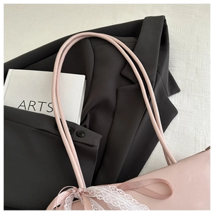 Detail of pink shoulder bag with delicate white lace trim and a satin bow on a suit