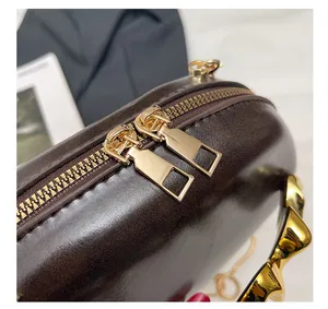 Macro view of dark brown polished leather bag with golden double zippers and chain detail
