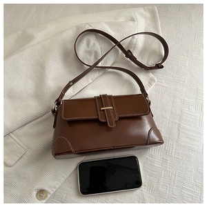 Detail view of deep brown vintage crossbody bag with metal buckle and smartphone for scale