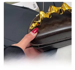 Close-up of precise stitching and gold wavy metal handle on dark brown leather bag