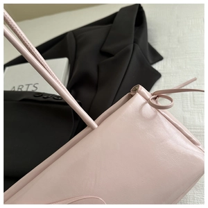 Detailed view of pink leather handbag side featuring a delicate bow-tie knot and fine texture