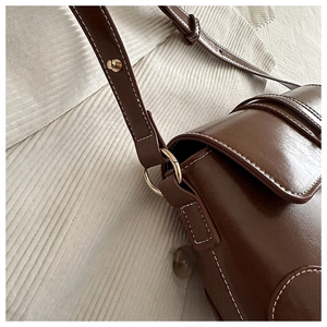Detail of dark brown vintage leather bag with contrast white stitching and gold hardware