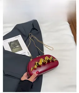 Macro detail of wine red handbag featuring bold wavy gold metal clasp and chain