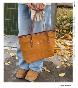Detail of a brown suede tote bag featuring a gold bow accent and dark leather handles