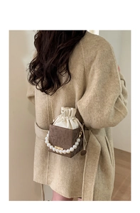 Detail of cube-shaped bucket bag with pearl handle and metal strap on model coat