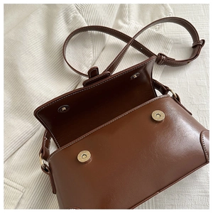 Detail of brown vintage leather crossbody bag featuring magnetic snaps and white stitching